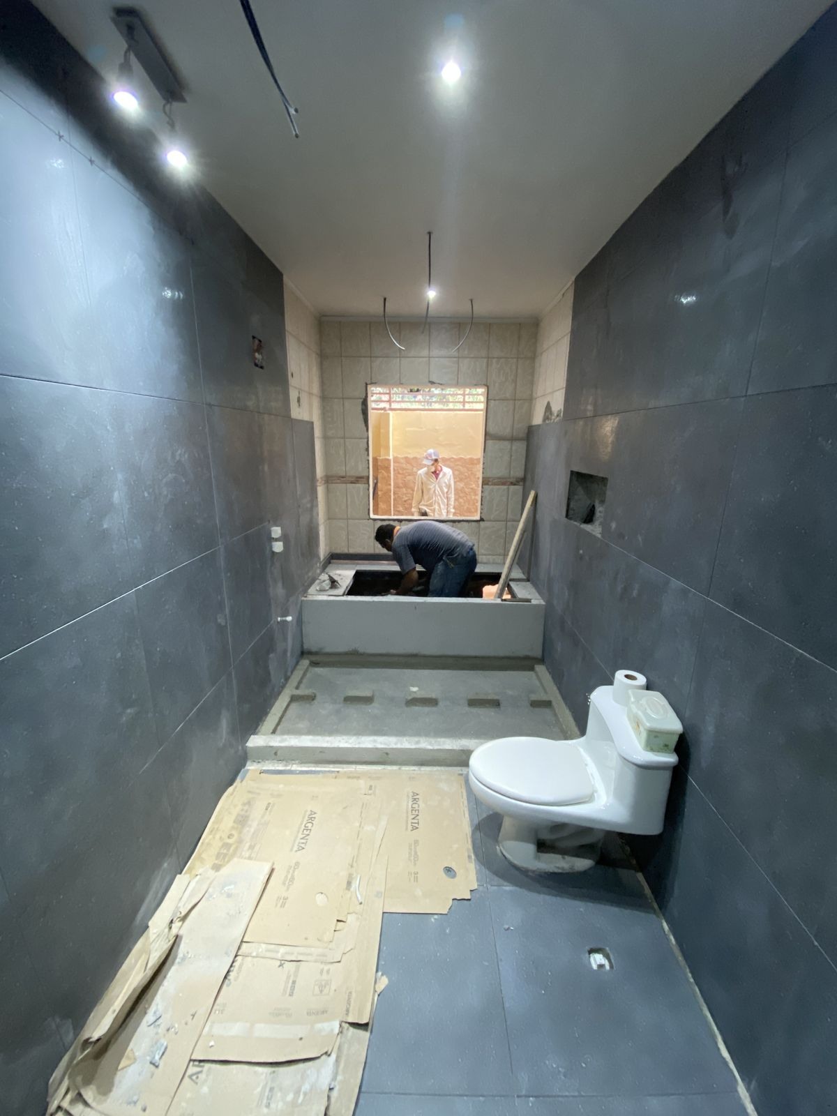 Casa de banho em remodelação, com azulejos cinzentos, banheira em construção e sanita instalada