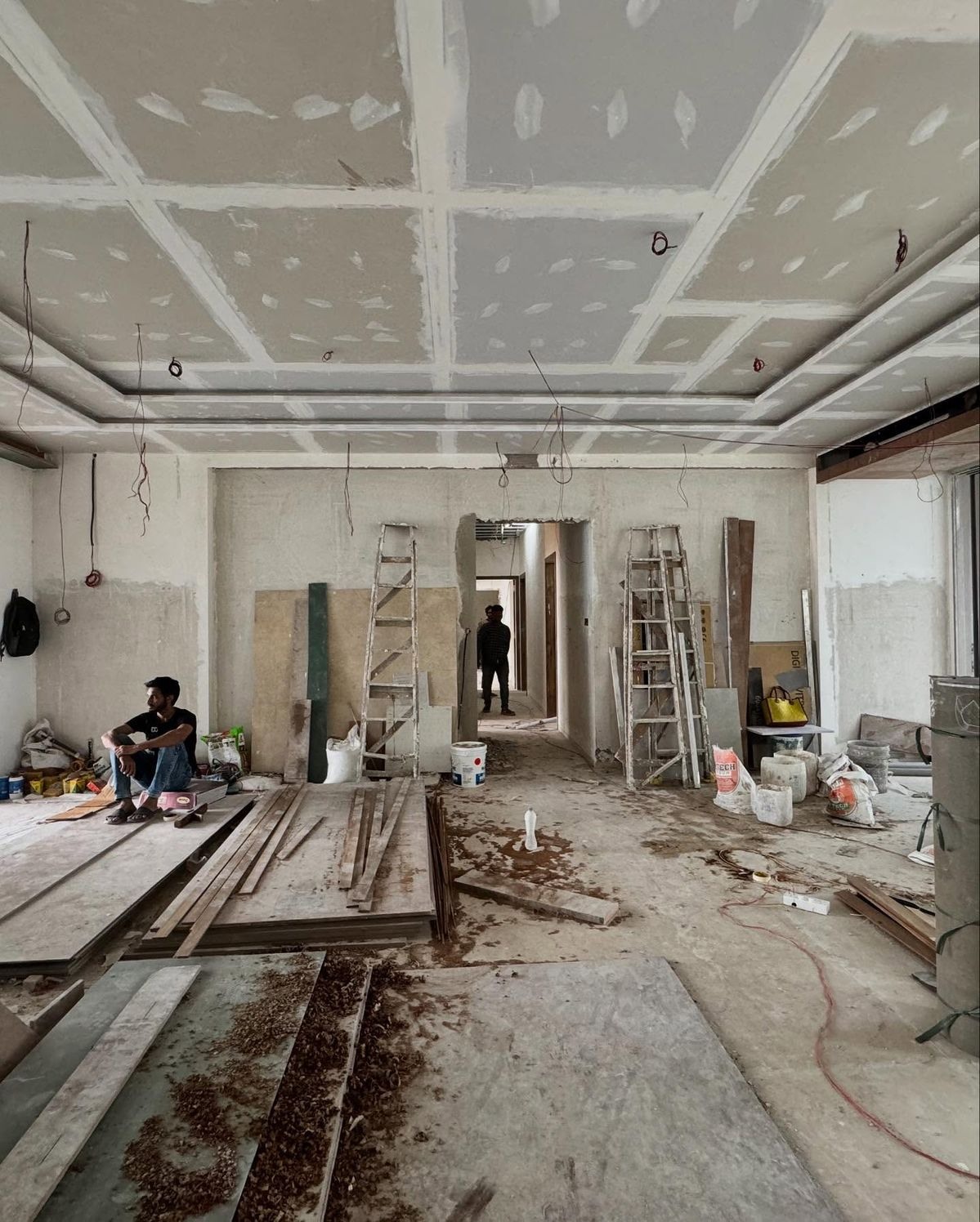 Divisão ampla em remodelação, com teto falso por acabar, escadotes, materiais e trabalhadores