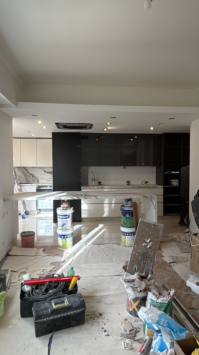 Cozinha em remodelação, com ilha revestida, armários pretos e brancos e latas de tinta